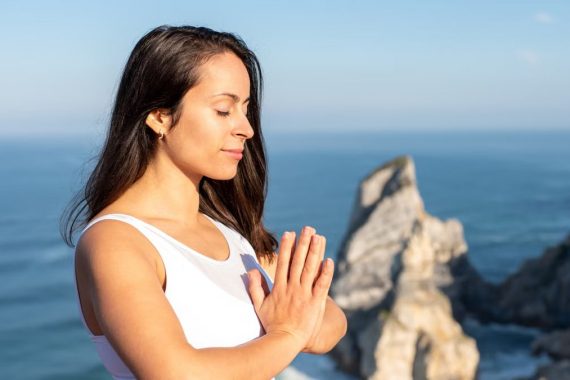 A woman meditates peacefully by the ocean in Portugal, embracing wellness.